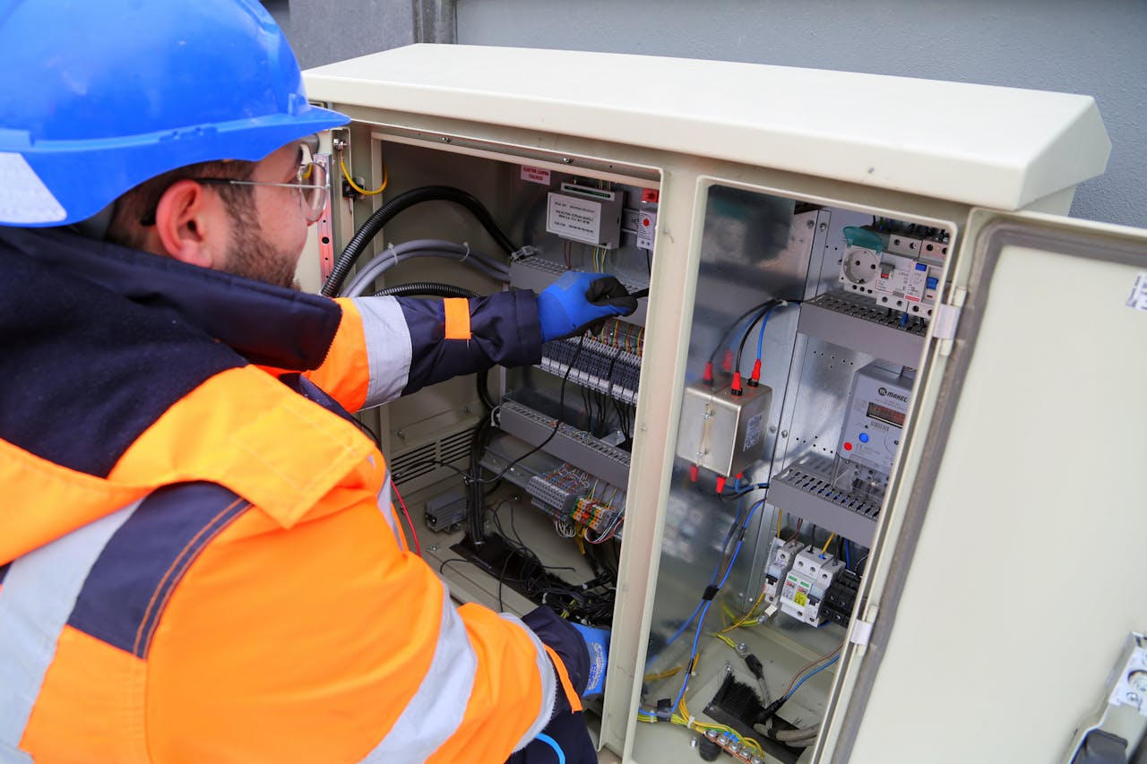 Engineer in safety gear working on an outdoor electrical panel, ensuring system functionality.